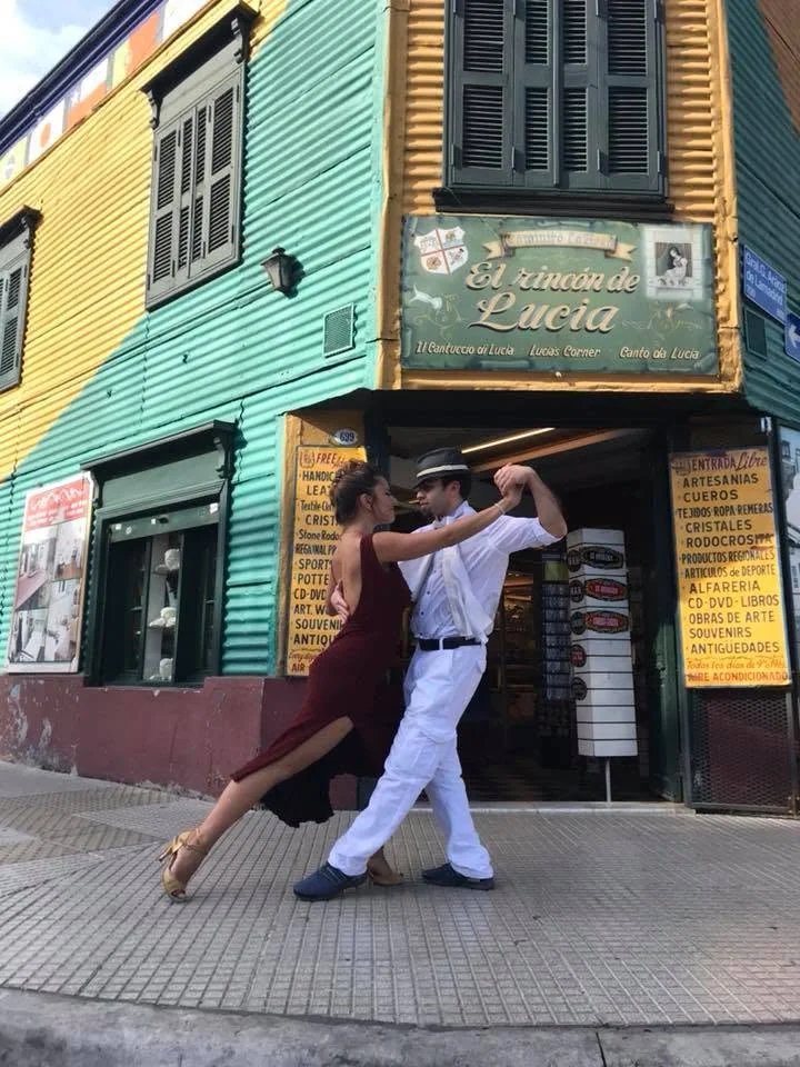 A tango duet on a street in front of brightly coloured buildings.